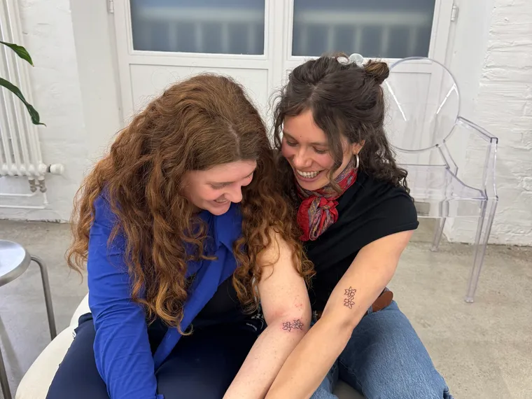 Sarah and a client leaning in over her arm, talking through placement