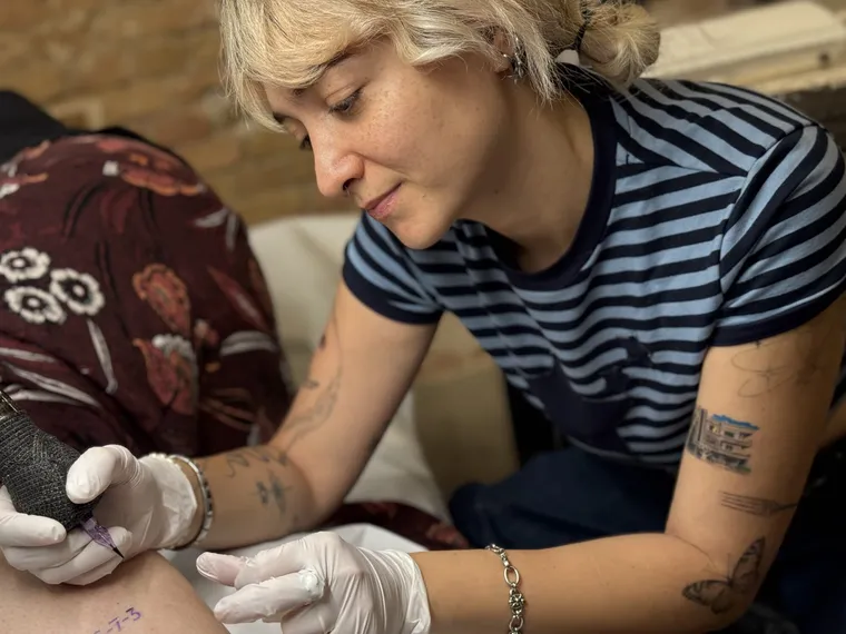 Sarah tattooing a fine-line piece, gloved and working close