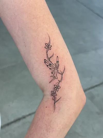 Winged figure among fine-line blossoms, trailing down the forearm